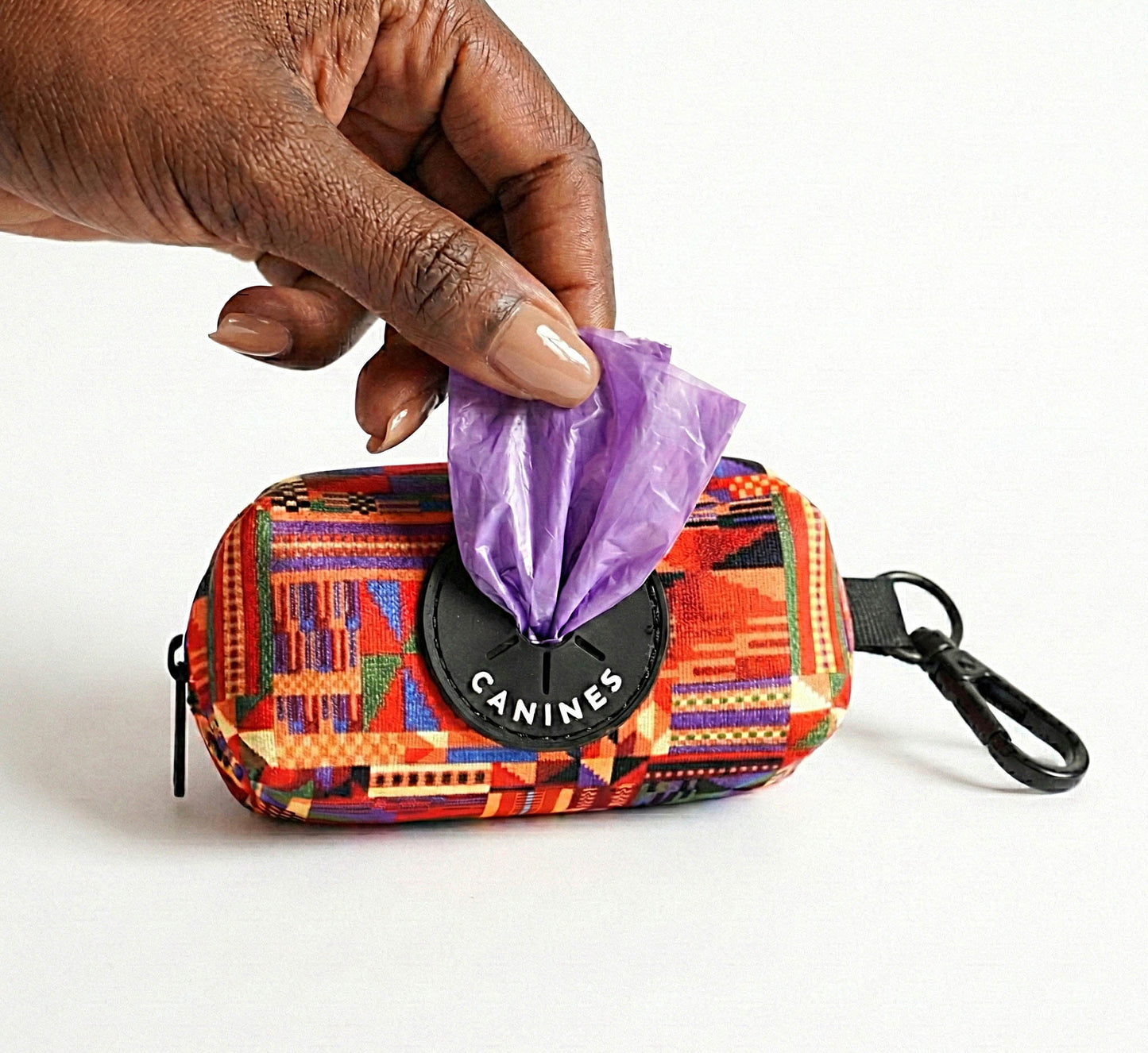 Kente Canines Safari Sunset red dog waste poop bag dispenser with a hand pulling out a purple bag on a white background